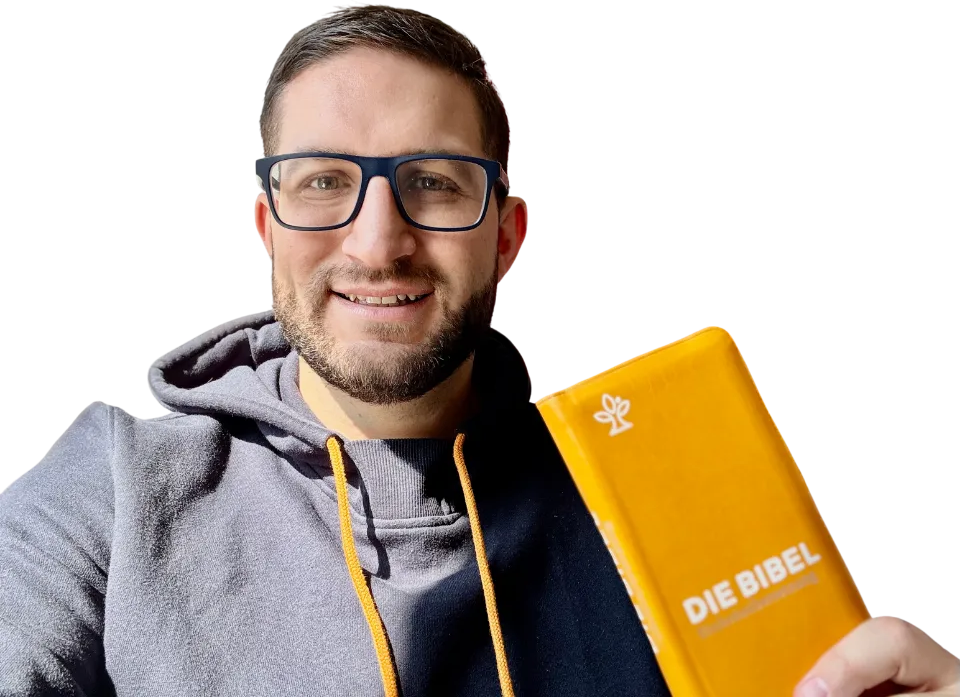 Nikola Baskarad lächelt und hält eine gelbe Bibel in die Kamera